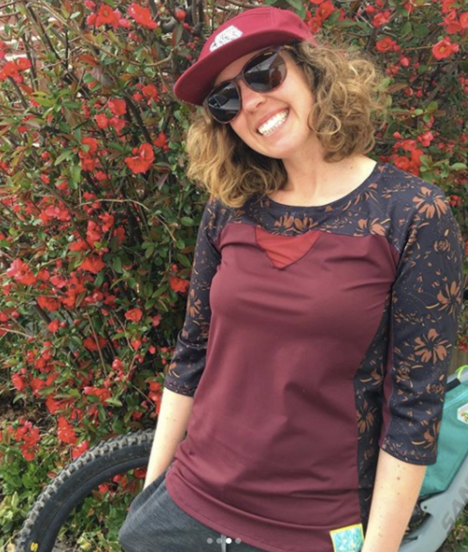 Model wearing a burgundy Rock Roselle top near red flowers
