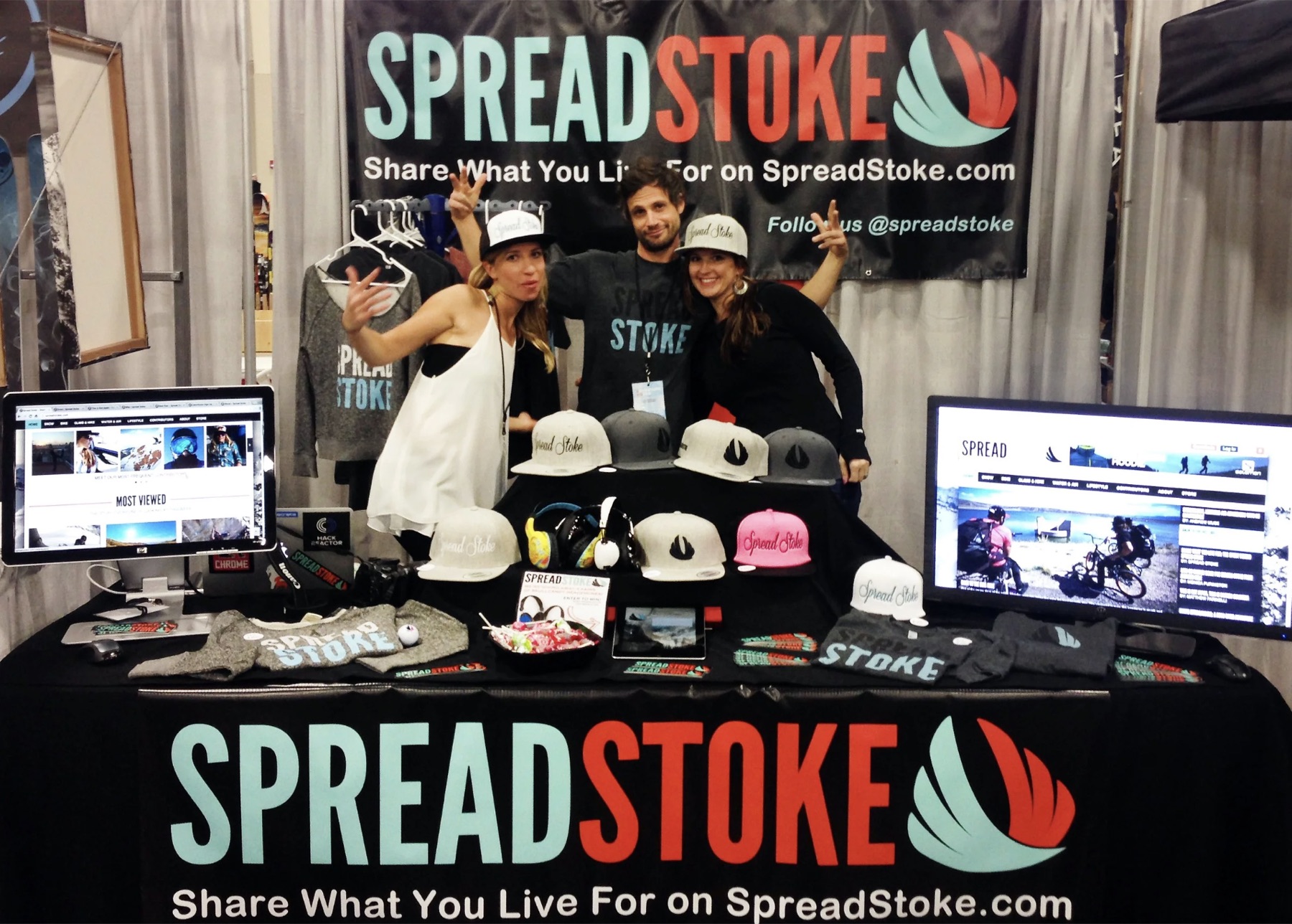Spread Stoke event booth with screens, hats, and branded banner